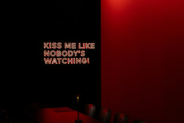 A dark bedroom glows with a pink and blue neon sign mounted on the wall, creating a moody aesthetic lighting display.