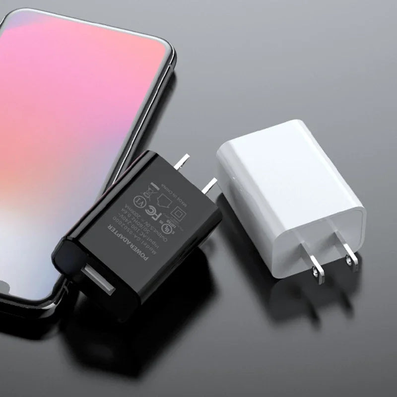 Black and white USB-A wall chargers beside a smartphone