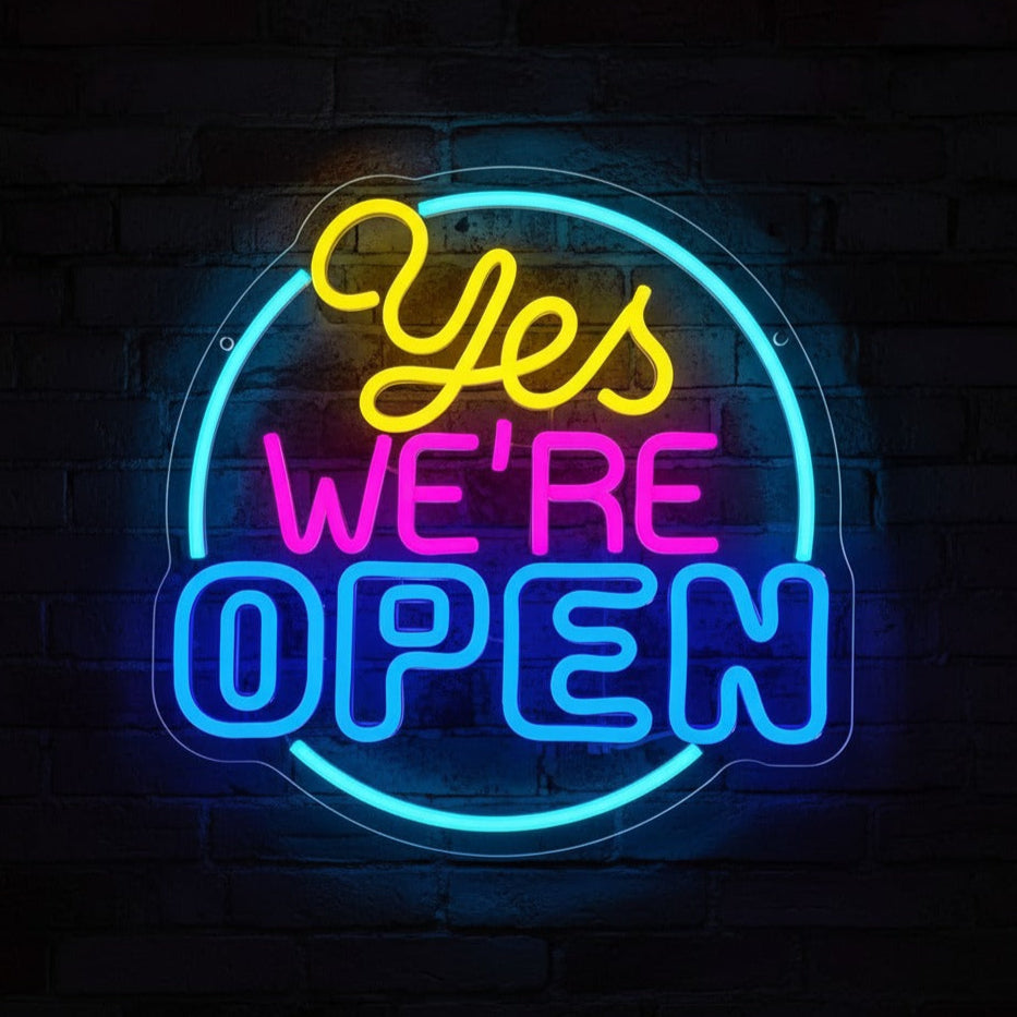 Neon sign with 'Yes We're Open' text on a brick wall background